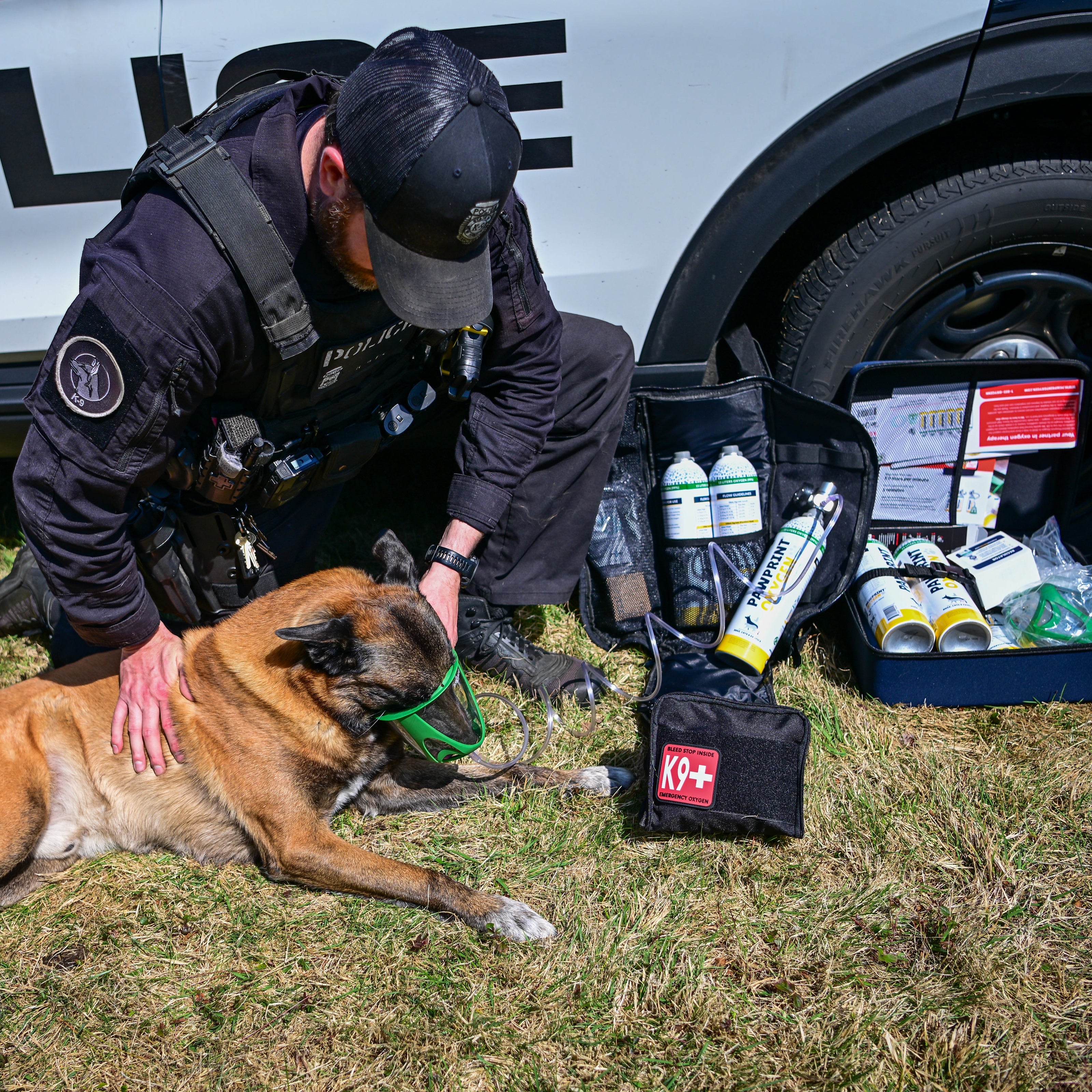 k9 police administering oxygen to k9 on the ground by police car