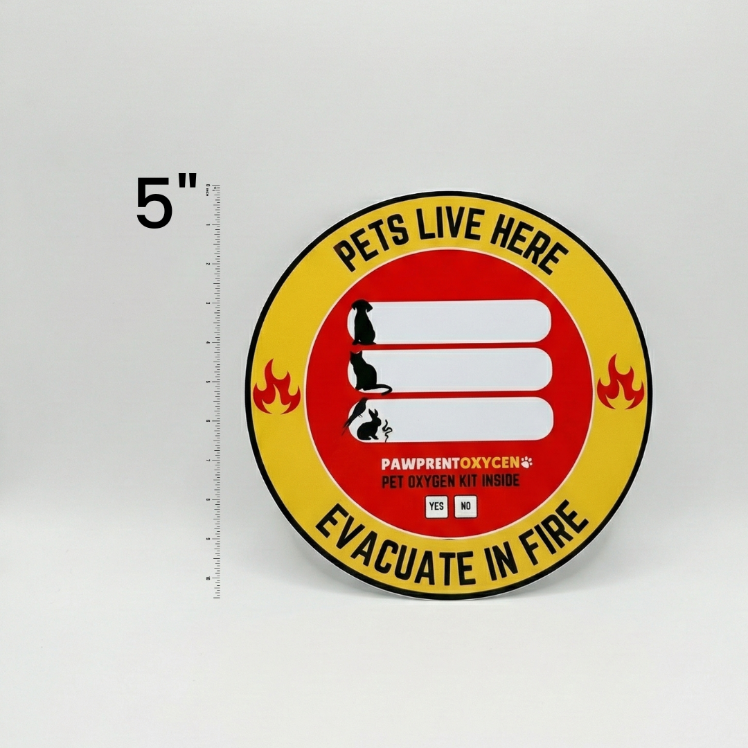 Round fire safety window sticker shown next to a ruler labeled ‘5″’, featuring the text ‘PETS LIVE HERE’ at the top and ‘EVACUATE IN FIRE’ at the bottom, with ‘PAWPRENTOXYGEN® PET OXYGEN KIT INSIDE’.