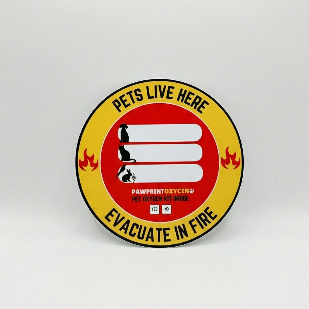 Round fire safety window sticker with yellow and red design reading ‘PETS LIVE HERE’ at the top and ‘EVACUATE IN FIRE’ at the bottom, featuring the text ‘PAWPRENTOXYGEN PET OXYGEN KIT INSIDE’.