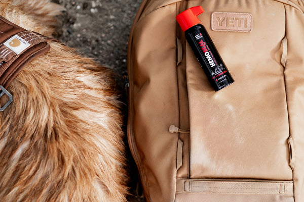 Black spray can with red nozzle on a beige backpack next to a furry animal.